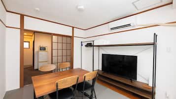 Un espacio habitable compacto con una mesa de comedor de madera, sillas negras, un televisor y una kitchenette.