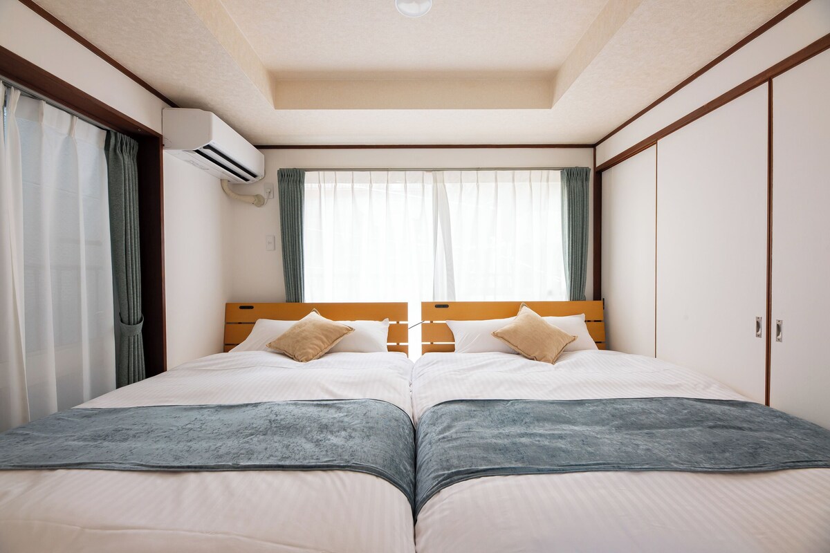 Uma cama de casal com cabeceira de madeira, duas almofadas e um cobertor cinza.