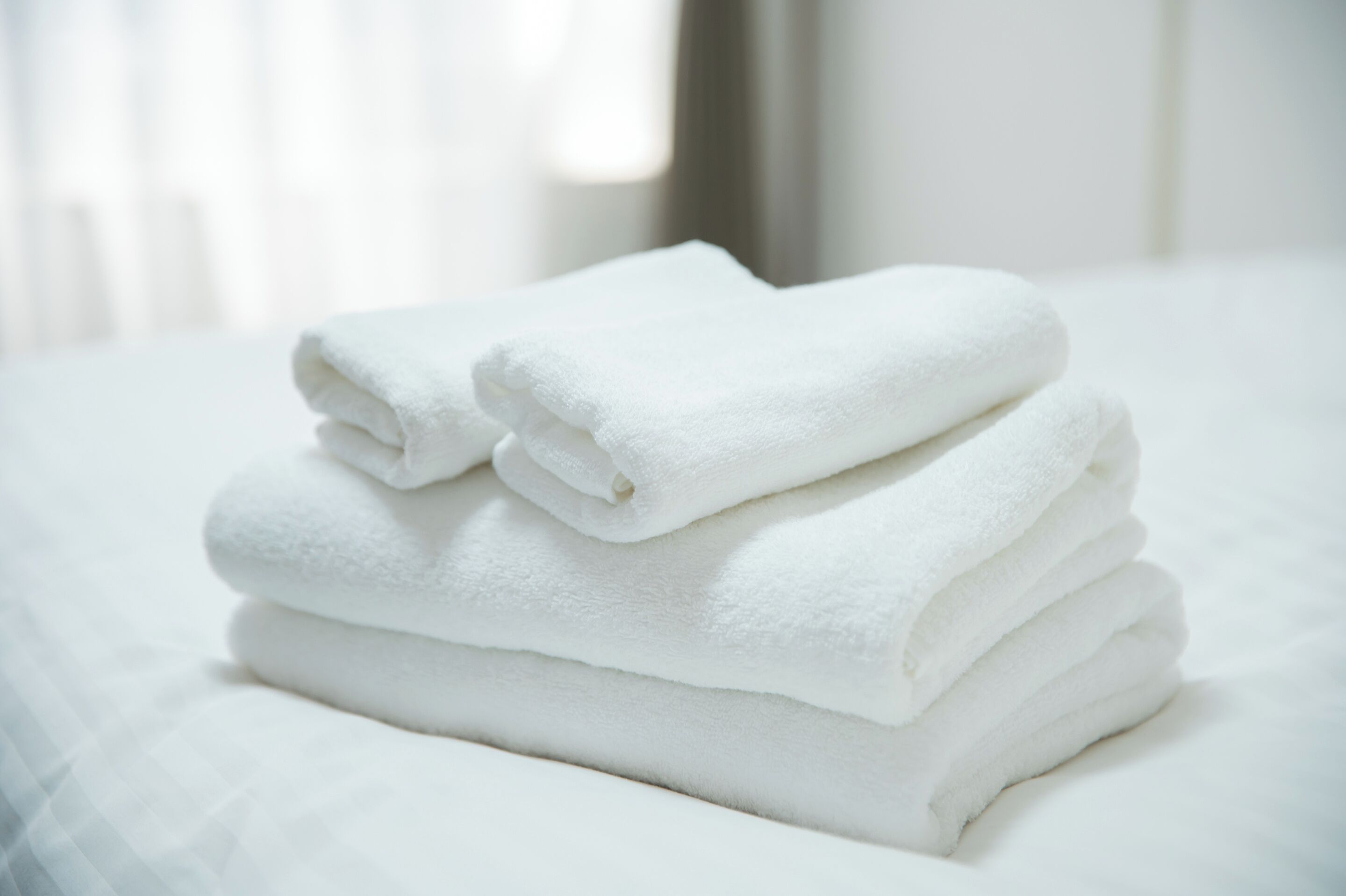 A stack of white towels on a bed.