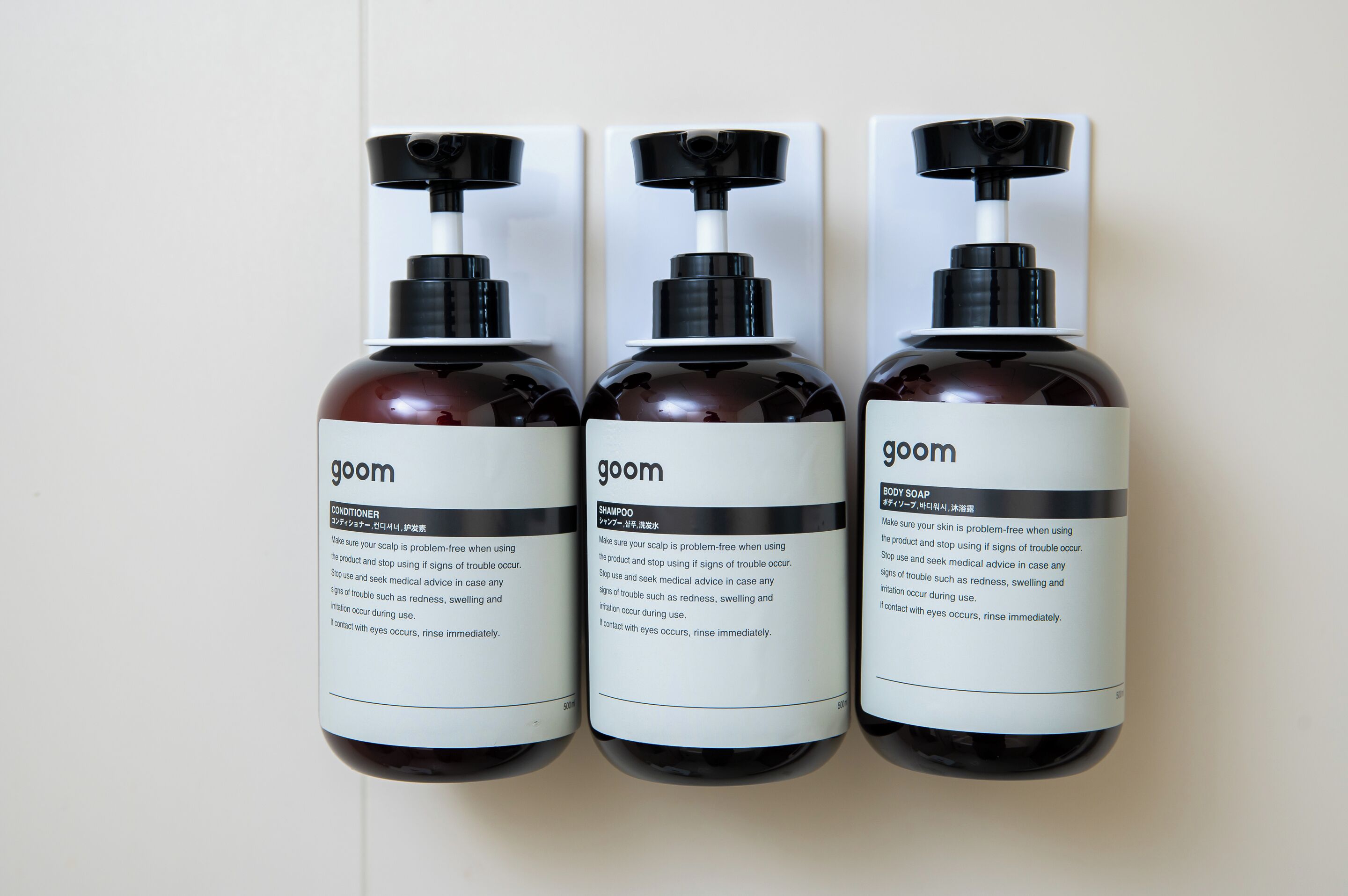 Three bottles of Goom body soap with pump dispensers, each labeled with usage instructions.