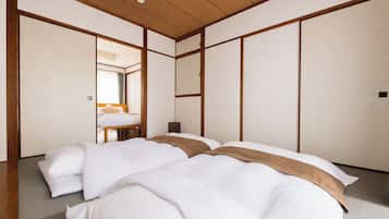 A traditional Japanese-style hotel room with tatami flooring, a low wooden ceiling, and a bed with white bedding and a brown accent.