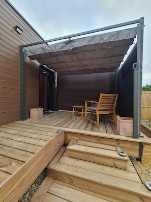 A wooden deck with a covered seating area, a chair, and a table. - Tiny House - Studio (Eygurande-et-Gardedeuil)