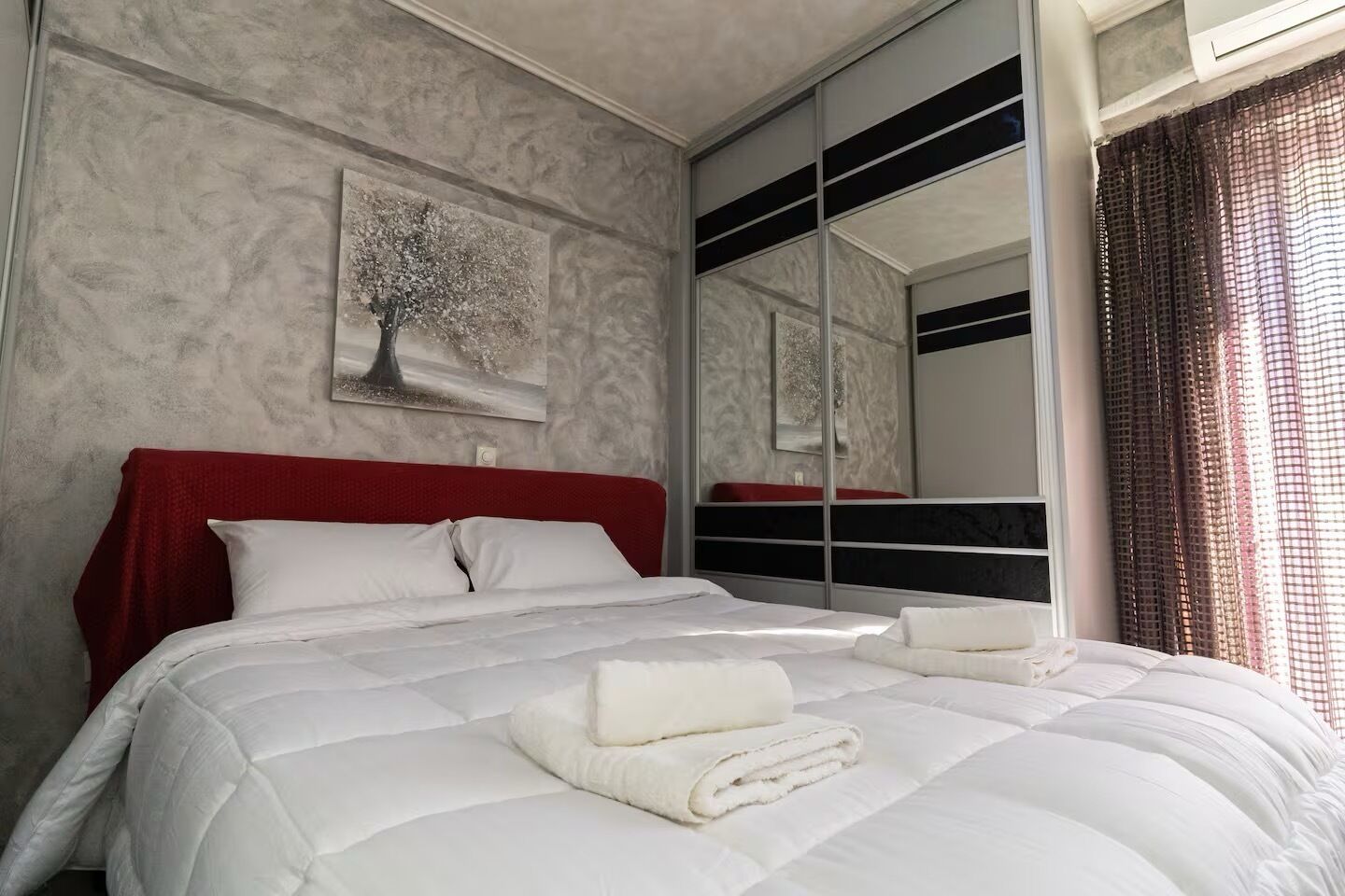 A hotel room with a large bed, a red headboard, a wall-mounted artwork, and a mirror reflecting the room.