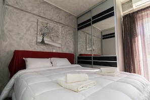 A hotel room with a large bed, a red headboard, a wall-mounted artwork, and a mirror reflecting the room.