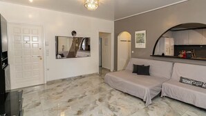 A modern living room with a sofa, a large mirror, and a chandelier. - Coastal Haven οf Piraeus - by ΜΡS (Pireas)