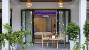 A modern outdoor seating area with a table and chairs, surrounded by potted plants and a glass door leading to a room. - Hoi An Ocean Waves Homestay (Da Nang)