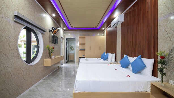 A hotel room with two beds, a round window, a wooden wardrobe, and a bathroom with a mirror. - Hoi An Ocean Waves Homestay (Da Nang)