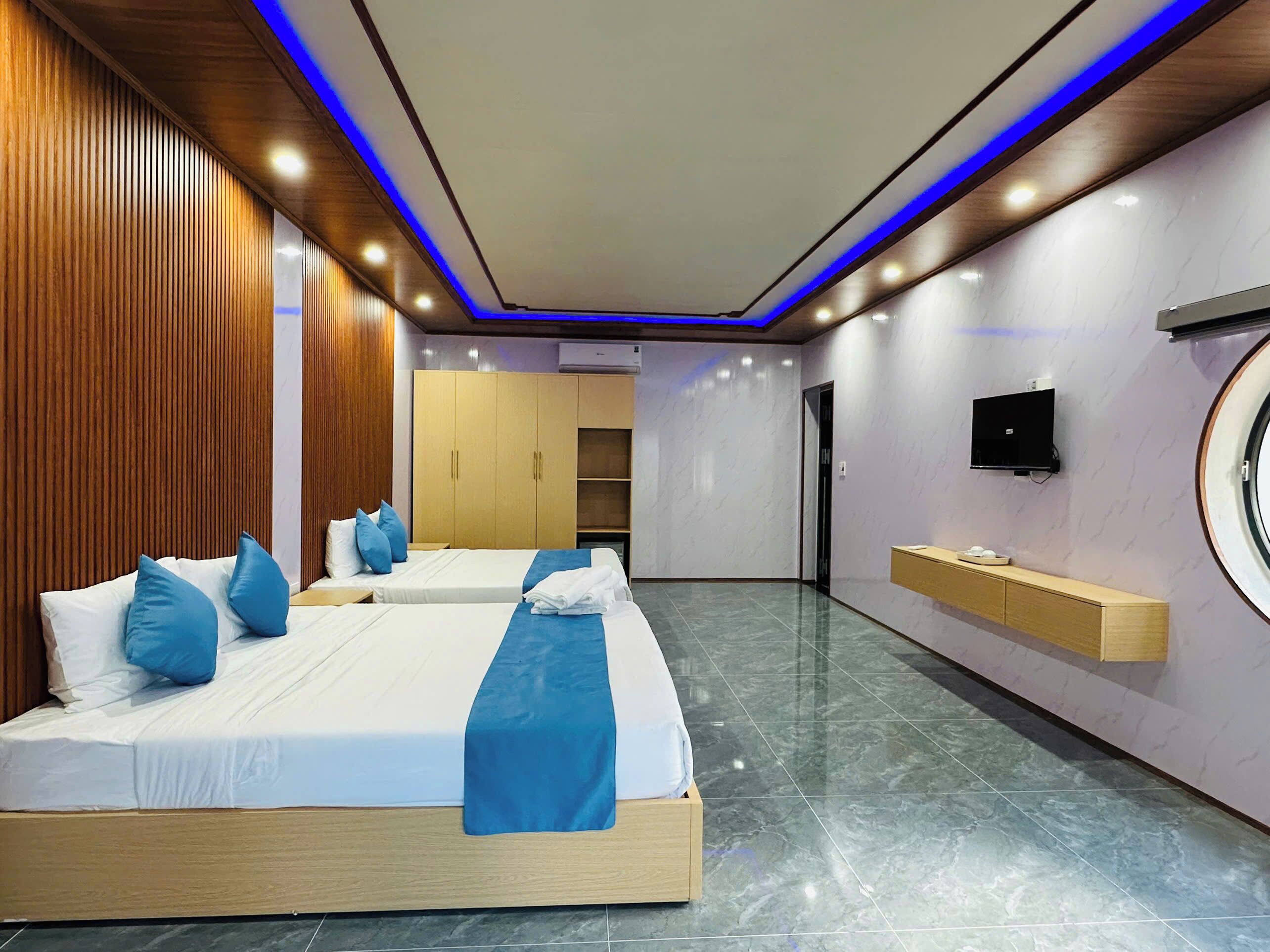 A hotel room with two beds, a TV, a minibar, and a circular window.