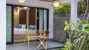 A modern bedroom with a sliding glass door, a bed with blue pillows, a wooden chair, and a small table with drinks and a plant. - Hoi An Ocean Waves Homestay (Da Nang)