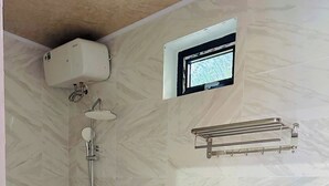A bathroom with a toilet, a shower with a handheld showerhead, a towel rack, and a small window. - Hoi An Ocean Waves Homestay (Da Nang)