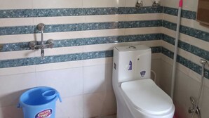 Un baño pequeño con inodoro, calentador de agua y un cubo azul.