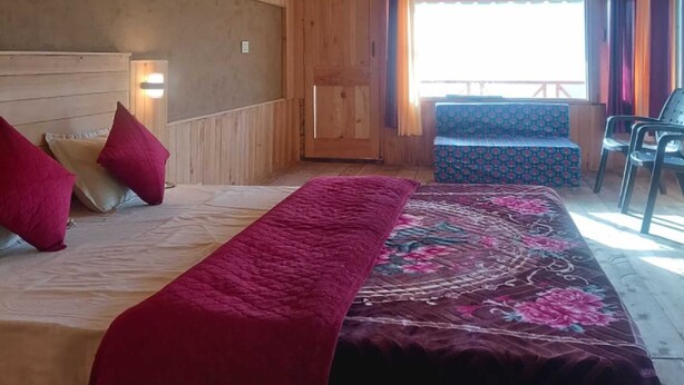 Un dormitorio de cabaña de madera con una cama, almohadas, un banco y vistas al exterior.