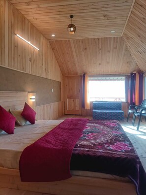 Une chambre aménagée dans une cabane en bois, avec un lit, des oreillers, un banc et une vue sur l’extérieur.
