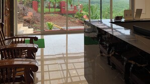 Amplia habitación con ventilador de techo, un gran ventanal que ofrece vistas a un paisaje exuberante y una zona de bar con una computadora portátil y una revista.