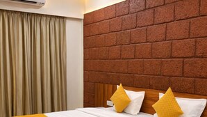 Habitación de hotel con cama, cabecera, ventilador de techo y ventana con cortinas.