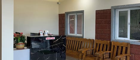 Un área de recepción con mostrador de mármol, sillas de madera, ventilador de techo y suelo de baldosas.