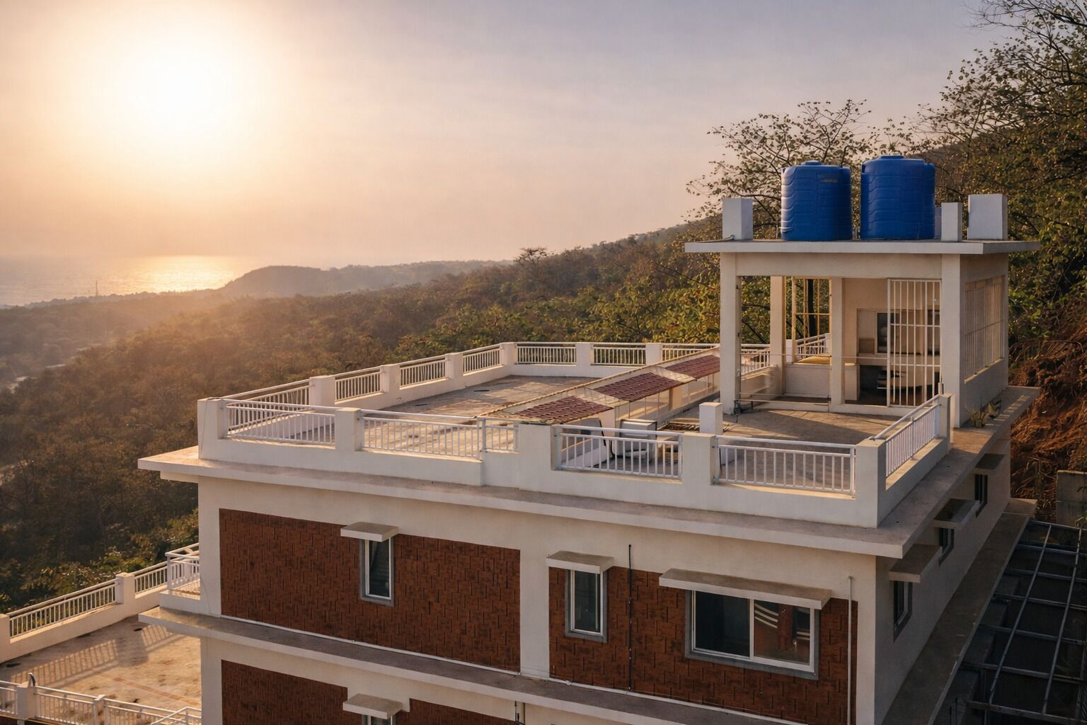 A multi-story building with a rooftop terrace, a water tank, and a view of a valley.