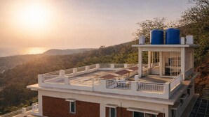 Un edificio de varios pisos con terraza en la azotea, un tanque de agua y vistas a un valle.