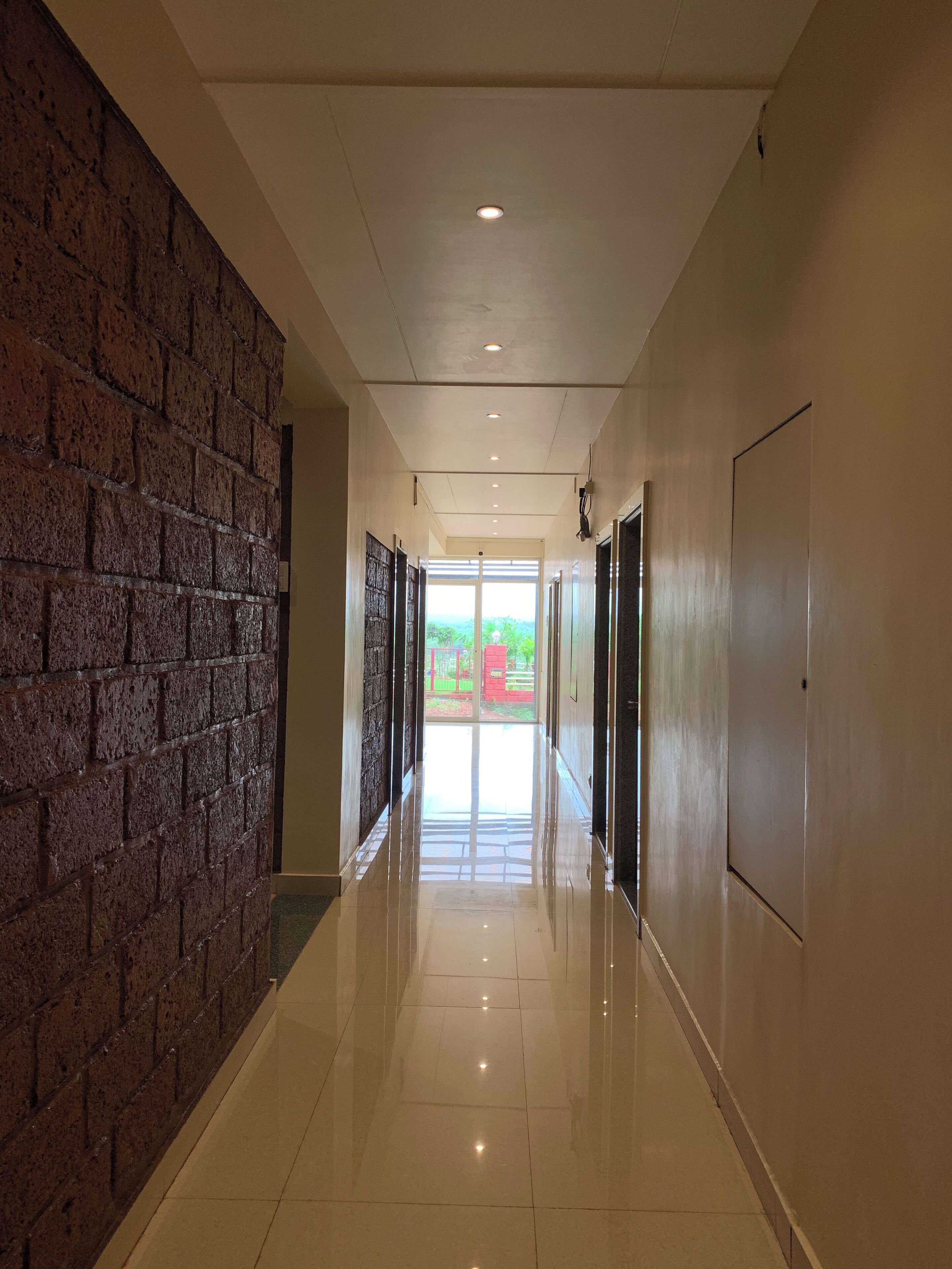A corridor with a brick wall on one side and a plain wall on the other, leading to a bright exit.
