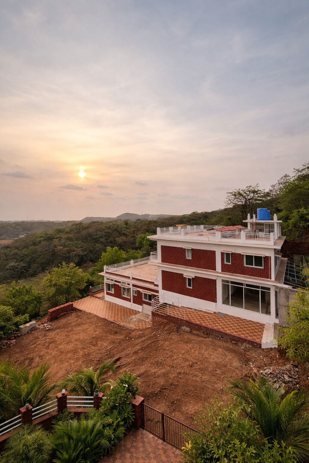 A two-story building with a flat roof, surrounded by greenery and hills.