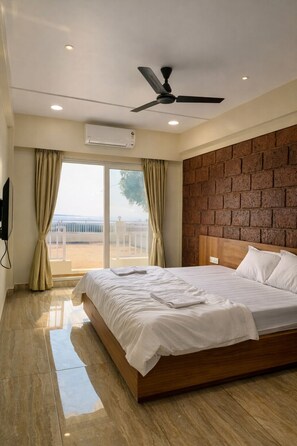 A hotel room with a bed, a ceiling fan, a view through a window, and a brick wall. - Anandi Hotel Guhagar (Guhagar)