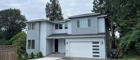 A two-story residential building with a garage, a driveway, and a wooden fence.
