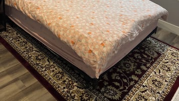 A bed with a floral bedspread, a patterned rug, and a window with sheer curtains.