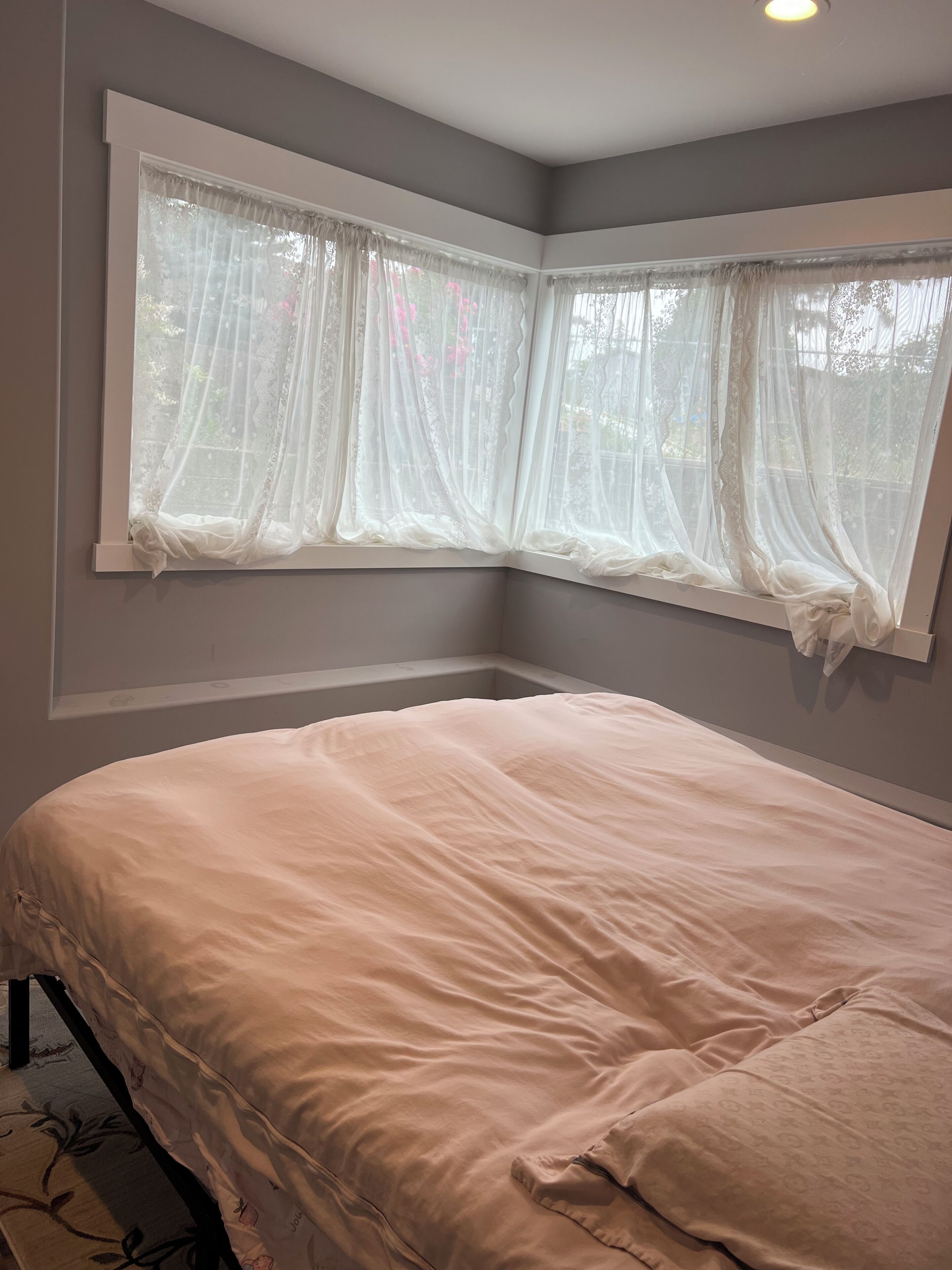 Une chambre à coucher avec un lit, une fenêtre avec des rideaux légers et un luminaire au plafond.