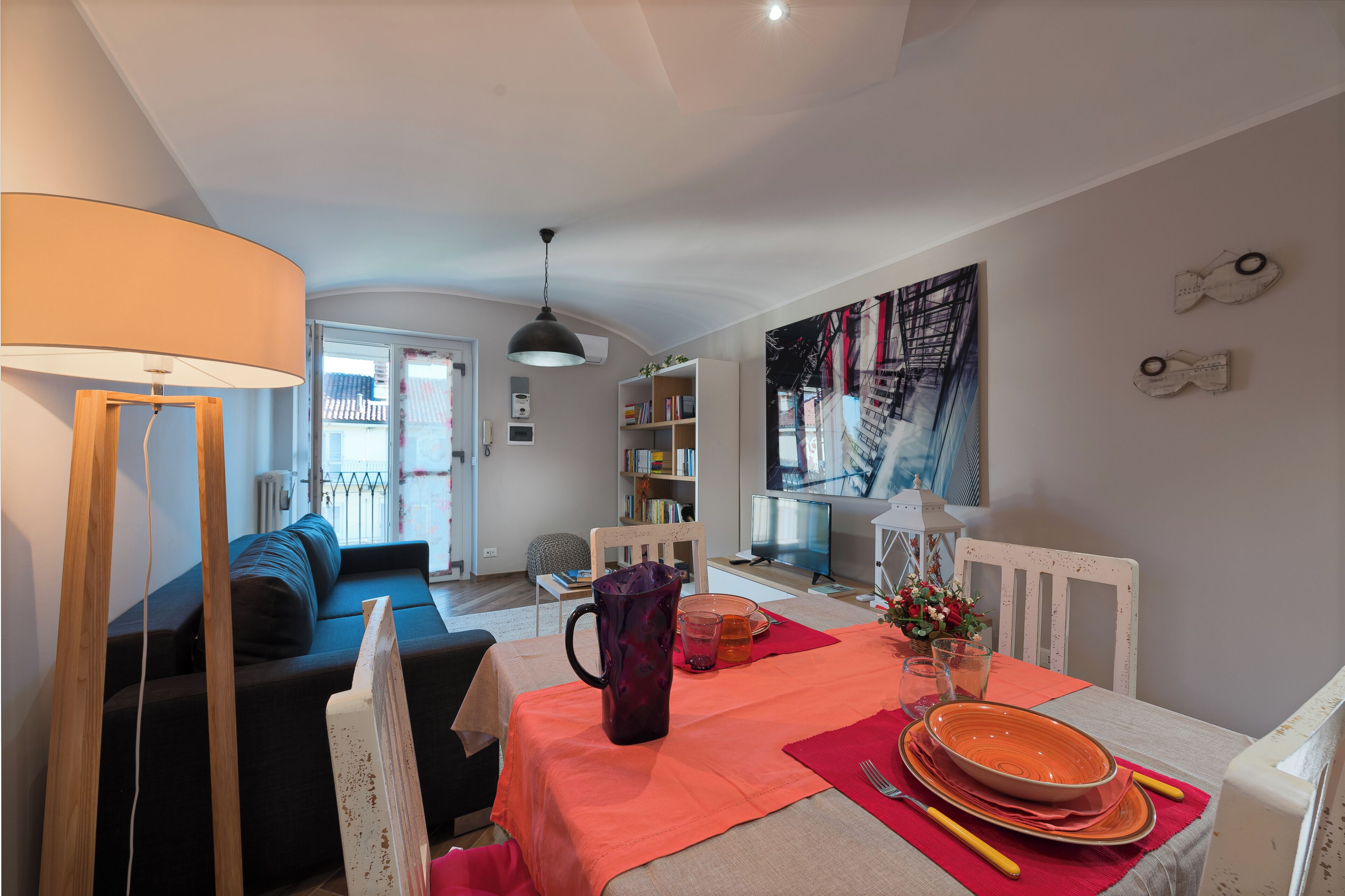 A dining area with a table set for two, a sofa, and a bookshelf in the background.