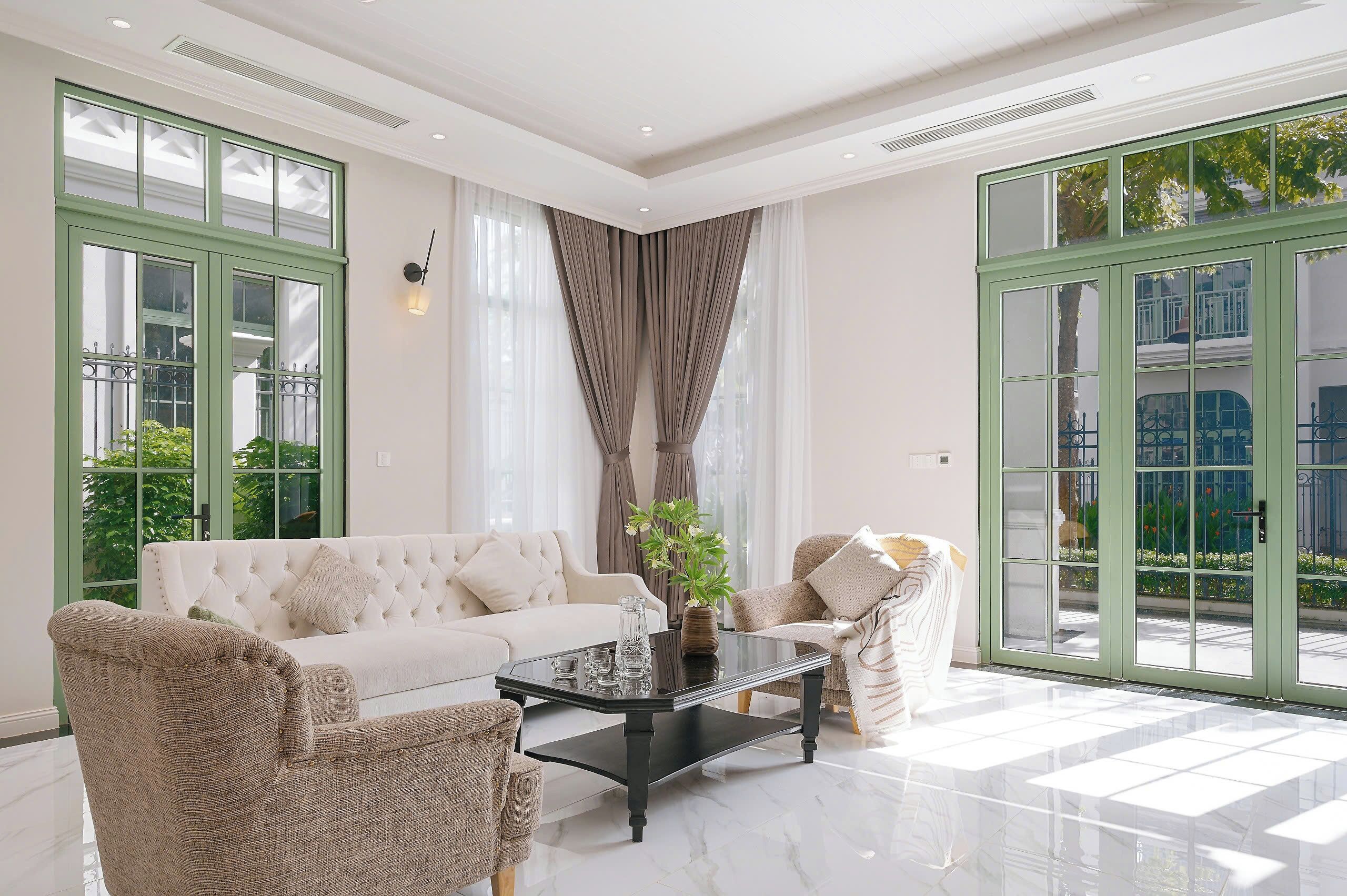 A spacious living room with a white sofa, two armchairs, a black coffee table, and a large window with a view of greenery.