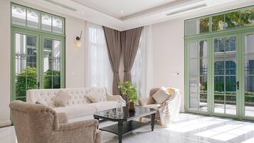 A spacious living room with a white sofa, two armchairs, a black coffee table, and a large window with a view of greenery.
