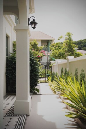 A pathway leading to a house with a tiled entrance, a black lantern, and a gated area with greenery.