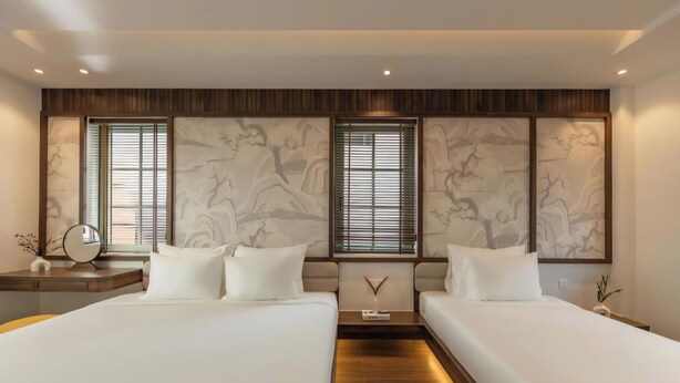 A hotel room with two beds, a wooden floor, a large window with blinds, and a decorative wall panel. - Ngoc Khanh Villas Bai Khem Phu Quoc (Phu Quoc)
