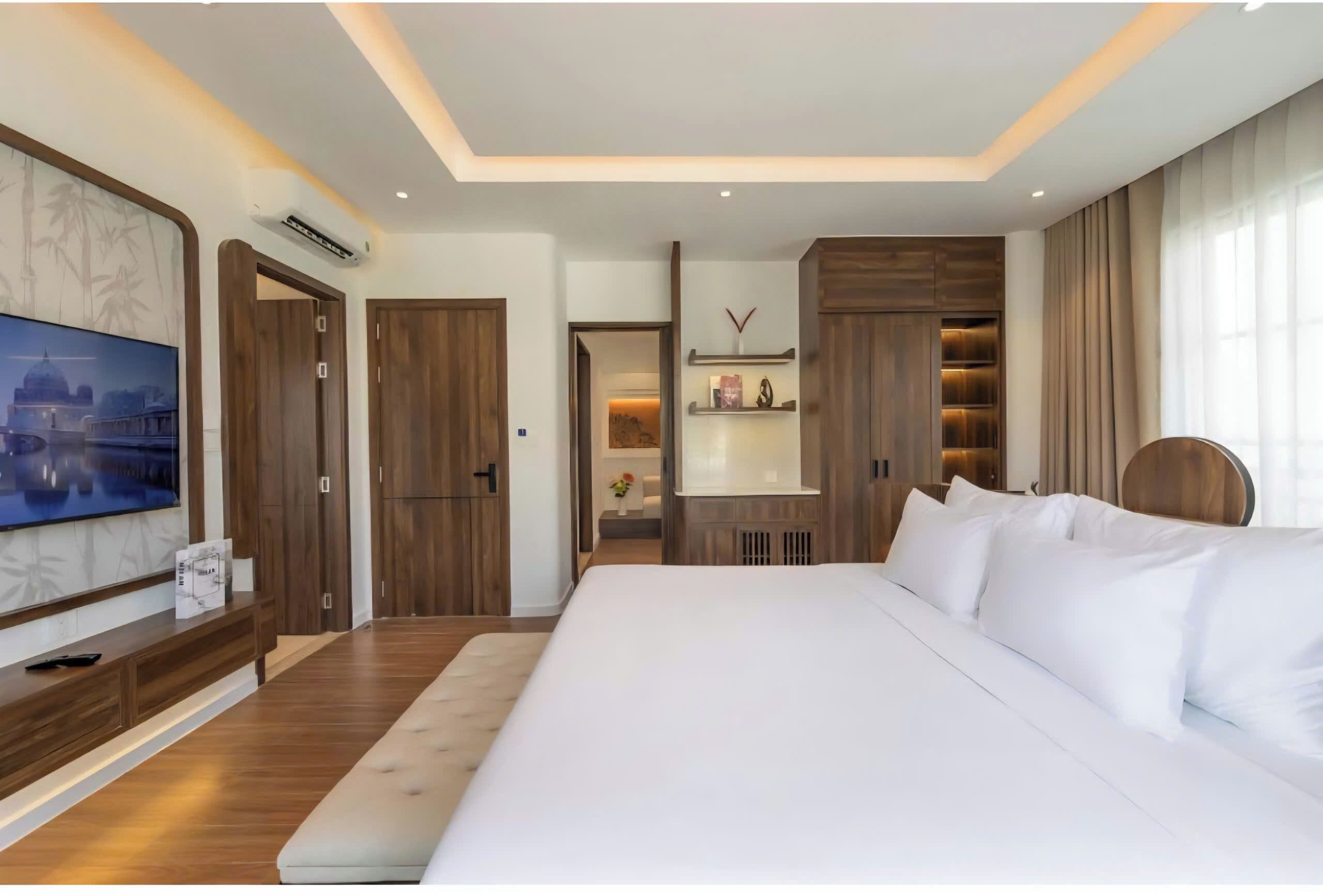 A hotel room with a large bed, a TV mounted on the wall, wooden doors, and built-in shelves.