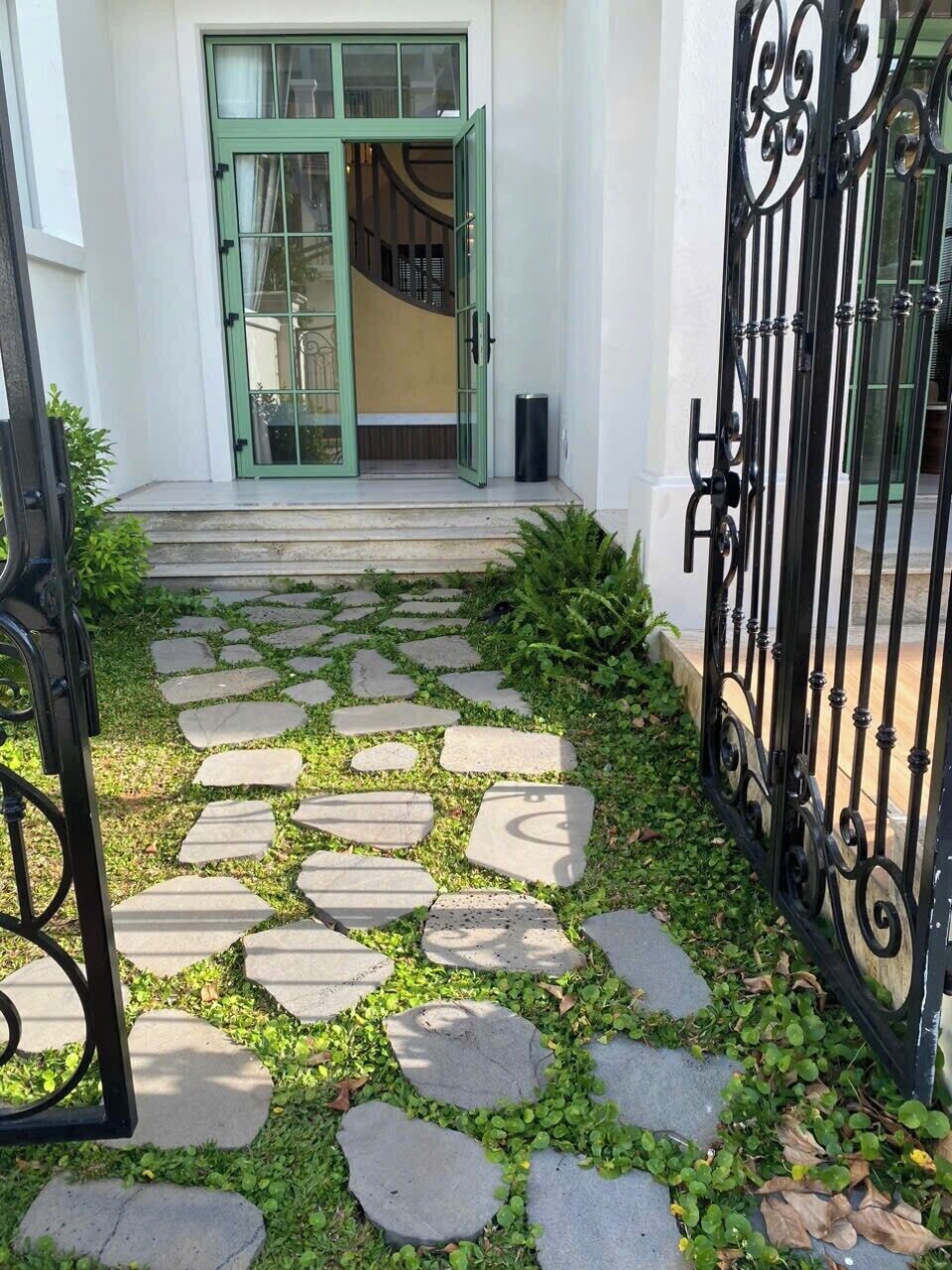 Un vialetto conduce all'ingresso di un edificio con una porta verde e un cancello in ferro battuto nero.