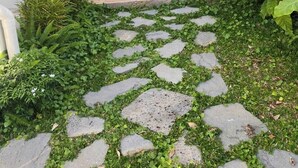 A narrow pathway with stone tiles and lush greenery, flanked by white buildings with green accents and traditional lanterns. - Ngoc Khanh Villas Bai Khem Phu Quoc (Phu Quoc)