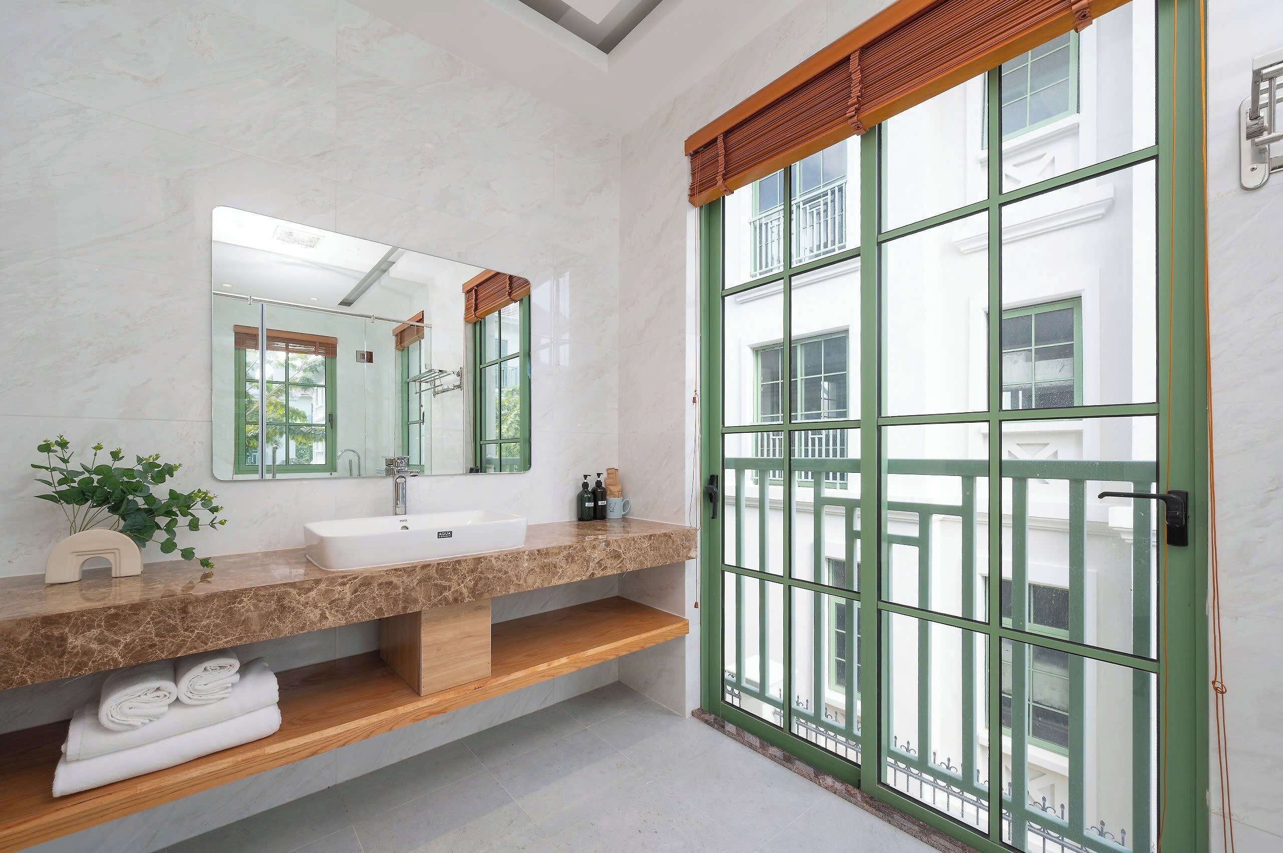 Ein Badezimmer mit Marmorplatte, Waschbecken, Spiegel und einem Fenster mit grünem Rahmen.