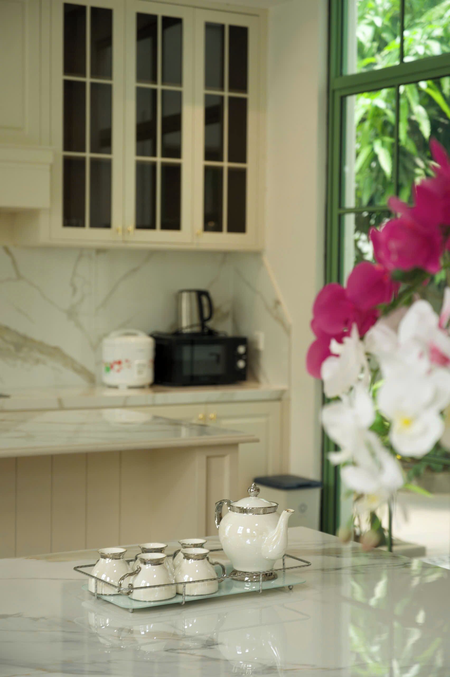 A kitchen with a marble countertop, a white teapot, and a set of white cups on a tray.
