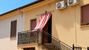 Um edifício com varanda, toldo listrado em vermelho e branco, e dois aparelhos de ar condicionado.
