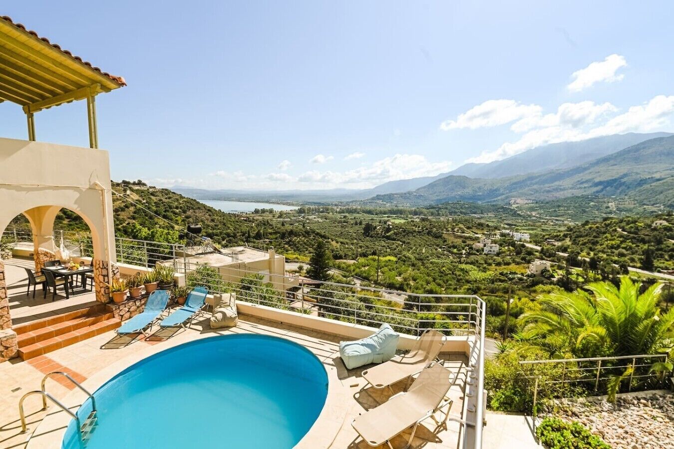 A pool area with lounge chairs and a table, overlooking a mountainous landscape.