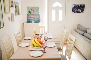 Een eetruimte met een tafel gedekt voor twee personen, inclusief borden, een fruitmand en een fles.