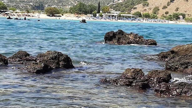 Eine Küstenlandschaft mit klarem Wasser, Felsenformationen und einem fernen Strand mit Gebäuden.