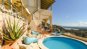 Ein Poolbereich mit Meerblick, Sitzgelegenheiten im Freien und einer Steinmauer.
