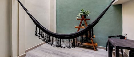 A hammock suspended between two walls in a room with a small window and a wooden ladder.