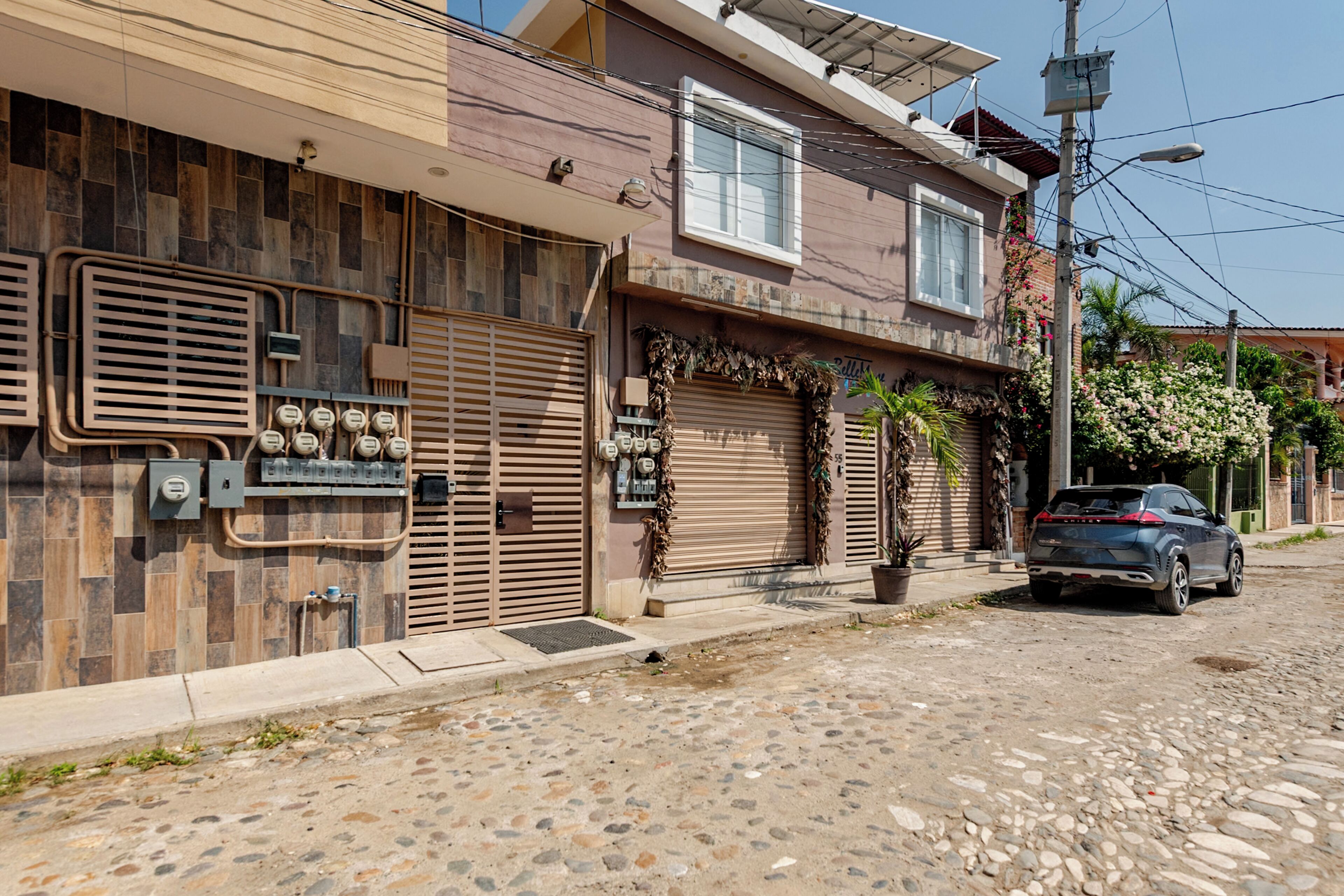 A building with a closed shutter, a car parked in front, and a street with cobblestones.