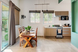 Eine moderne Küche mit einer zentralen Kochinsel, einem Essbereich mit Holzstühlen und Blick ins Freie durch das Fenster.