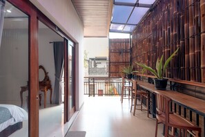 A room with a sliding glass door leading to a balcony, a wooden bench with potted plants, and a bamboo wall. - Cozzy Villa Mentari (Badung)