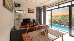 Una sala de estar moderna con televisor, sofá, mesa de comedor y vista a una piscina.