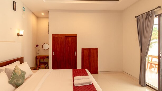 Habitación de hotel con cama, escritorio, silla, armario y puerta corrediza de vidrio al exterior.
