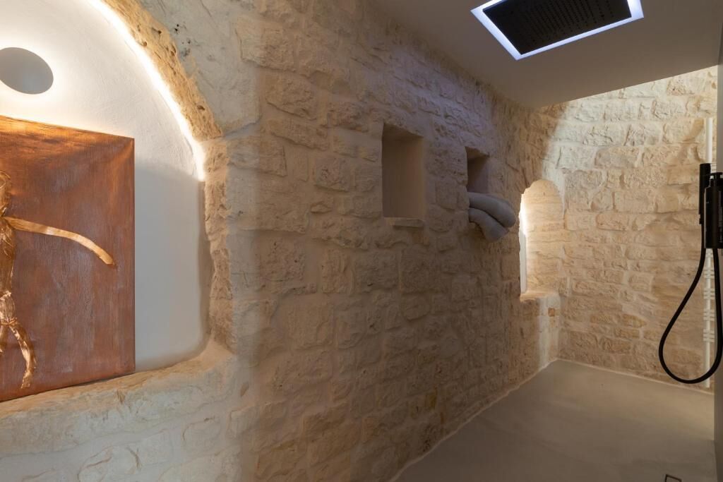 Una habitación con paredes de piedra, una escultura de madera, un banco empotrado y una zona de ducha.